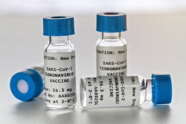 Coronavirus Covid-19 aşı konsepti - beyaz masa üzerinde mavi başlıklı küçük cam şişeler, yakın plan detay (sahte verili kendi çıkartma tasarımı - gerçek ürün değil)
