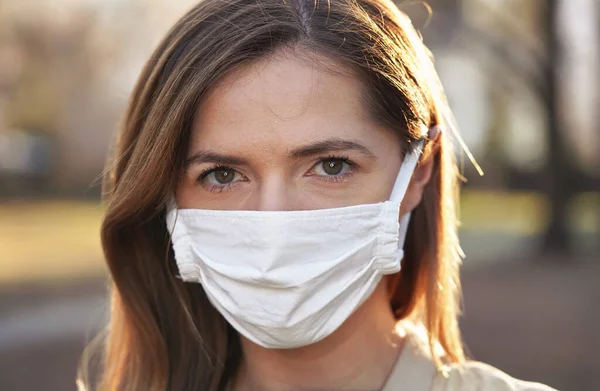 Young woman wearing white cotton virus mouth nose mask, nice blurred park bokeh in background, closeup face portrait