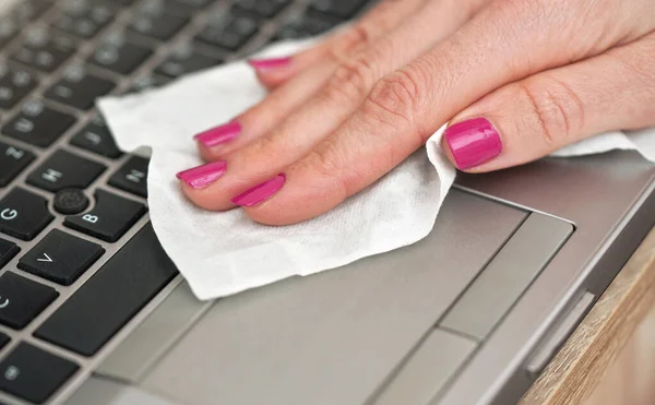 Woman cleaning laptop keyboard with white tissue, detail on her fingers holding paper towel - disinfection during coronavirus covid-19 concept