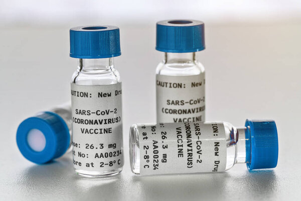Coronavirus Covid-19 vaccine concept - small glass vials with blue caps on white table, closeup detail (own sticker design with dummy data - not real product)