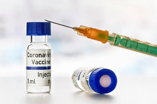 コロナウイルスCovid 19ワクチンのコンセプト 白い机の上に青いキャップを持つ2つの小さなボトル 緑のオレンジの注射器は 1の上に配置され クローズアップの詳細 — ストック写真
