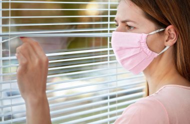 Pembe evdeki genç kadın dışarıdaki pencere perdelerinden bakarak pamuk virüsü maskesi yaptı. Karantina ya da Coronavirus covid-19 salgını sırasında evde kalmak