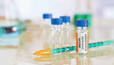 Coronavirus covid-19 aşı konsepti - parlak beyaz masa üzerinde mavi kapaklı küçük şişe, yanında yeşil turuncu şırınga, daha fazla laboratuvar camı bulanık arka plan (çıkartma kendi tasarımıdır - gerçek ürün değil)