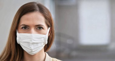 Beyaz pamuklu eli olan genç bir kadın yüz maskesi, yakın portre. Bulanık bina kapısı arka planı. Coronavirus covid-19 salgını önleme sırasında kullanılabilir