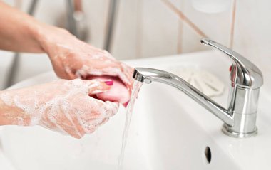 Genç bir kadın ellerini musluğun altında pembe sabunlukla yıkıyor. Köpüklü derinin detayları. Kişisel hijyen kavramı - koronavirüs 19 salgını önleme