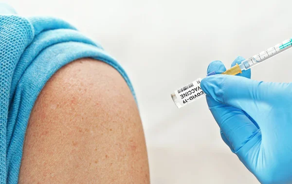 注射器とコロナウイルスワクチン ステッカー自身のデザイン ダミーバーコード を保持青い手袋で手 近くに座っている患者の肩にそれを注入しようとしています 詳細を閉じます Covid 19治療法の概念 — ストック写真