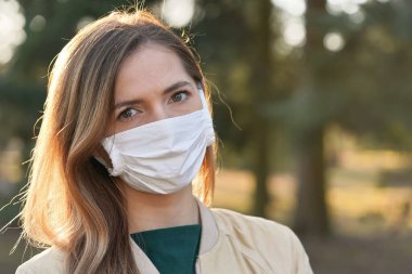 Beyaz pamuk virüsü takan genç bir kadın burun maskesi, bulanık park ve ağaçlar arka plan, yakın plan yüz portresi, Coronavirus covid 19 salgın önleme konsepti