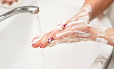 Genç bir kadın ellerini musluğun altında sabunla yıkıyor. Köpüklü derinin detayları. Kişisel hijyen kavramı - koronavirüs covid-19 salgını önleme