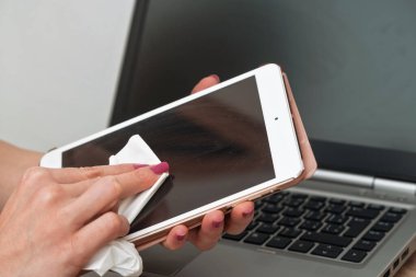 Kadın tableti pamuklu kağıt mendille temizliyor, siyah ekranı siliyor, yakın çekim detaylarıyla. Bulanık dizüstü bilgisayar klavye arka planı. Coronavirus covid-19 salgını önleme