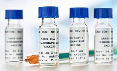 Coronavirus Covid-19 aşı konsepti - beyaz masa üzerinde mavi başlıklı küçük cam şişeler, yakın plan detay (sahte verili kendi çıkartma tasarımı - gerçek ürün değil)