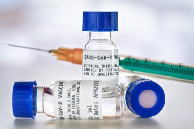 Coronavirus Covid 19 aşı konsepti - beyaz masa üzerinde mavi başlıklı küçük cam şişeler, yakın plan detay (sahte verili kendi çıkartma tasarımı - gerçek ürün değil)
