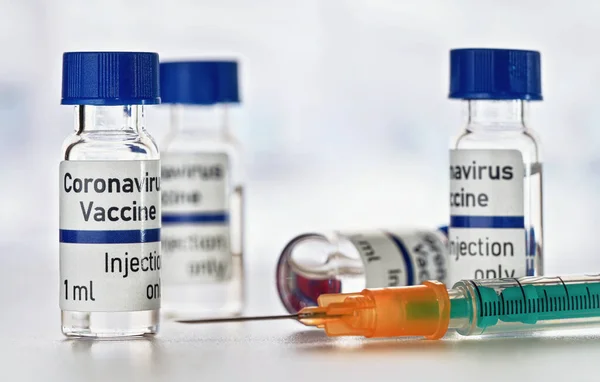 コロナウイルスCovid 19ワクチンのコンセプト 実際の製品ではなく独自のデザイン 白いテーブルの上に青いキャップを持つ小さなガラスのバイアル 近くの緑のオレンジの注射器 クローズアップの詳細 — ストック写真