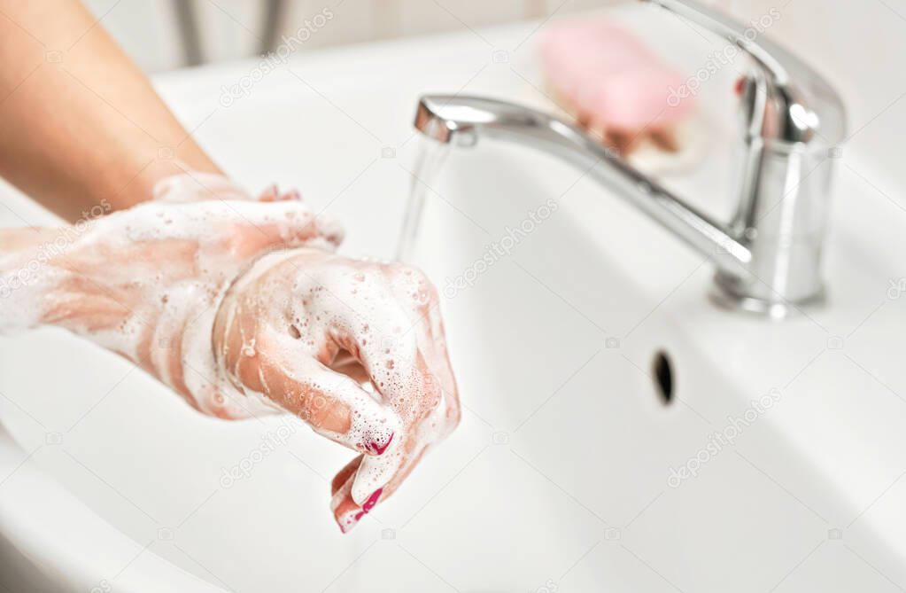 Young woman washing her hands under water tap faucet with soap. Detail on suds covered skin. Personal hygiene concept - coronavirus covid 19 outbreak prevention