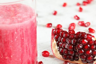 Nar meyvesi porsiyonu, beyaz tahtaya saçılmış böğürtlen gibi mücevher, yanında pembe meyve püresi olan bardak.