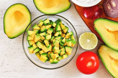 Avokado yarımları, limonlu domates ve soğan - beyaz çalışma tahtasında temel guacamole malzemeleri, yukarıdan görüş