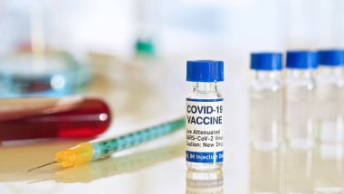 Coronavirus Covid 19 aşı konsepti (kendi tasarımı, gerçek ürün değil) - beyaz masa üzerinde mavi başlıklı küçük cam şişeler, yakın çekim detayı yeşil turuncu şırınga 