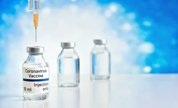 Coronavirus Covid-19 vaccine concept - glass vials with metal caps on white table, orange syringe needle above, closeup detail