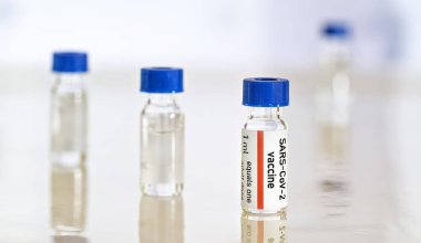 Coronavirus Covid 19 aşı konsepti - beyaz masa üzerinde mavi başlıklı küçük cam şişeler, yakın plan detay (sahte verili kendi çıkartma tasarımı - gerçek ürün değil)