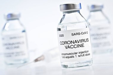 Coronavirus Covid-19 aşı konsepti - beyaz masada metal kapaklı cam şişeler, bulanık şırınga ve arka planda daha fazla şişe