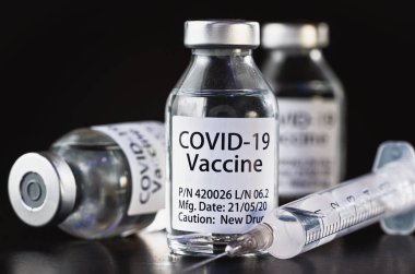 Coronavirus Covid-19 aşı konsepti - siyah masanın üzerinde üç cam şişe, yakınlarda şırınga iğnesi, yakın plan detayı (etiket tasarımı - sahte veri, gerçek ürün değil)