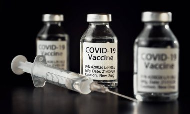 Coronavirus Covid-19 aşı konsepti - siyah masanın üzerinde üç cam şişe, yakınlarda şırınga iğnesi, yakın plan detayı (etiket tasarımı - sahte veri, gerçek ürün değil)