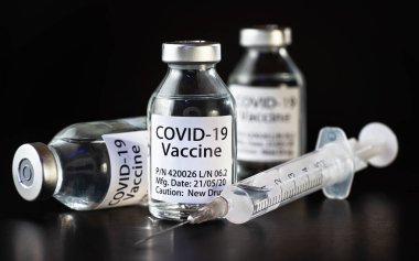 Coronavirus Covid-19 aşı konsepti - siyah masanın üzerinde üç cam şişe, yakınlarda şırınga iğnesi, yakın plan detayı (etiket tasarımı - sahte veri, gerçek ürün değil)