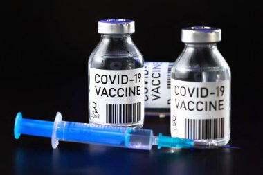 Coronavirus Covid-19 aşı konsepti - siyah masanın üzerinde üç cam şişe, yakınında şırınga iğnesi, yakın plan detayı (etiket tasarımı - sahte veri ve barkod, gerçek ürün değil)