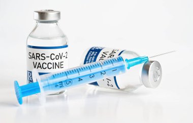 Coronavirus Covid-19 aşı konsepti (çıkartma kendi tasarımı, gerçek ürün değil) - beyaz masada metal kapaklı cam şişeler, şırınga iğnesi yanında