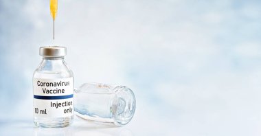 Coronavirus aşı konsepti, beyaz masanın üzerinde gümüş kapaklı cam şişe, enjekte edilecek turuncu şırınga şırıngası, sağ arka planda bulanık alan (çıkartma gerçek ürün değil)