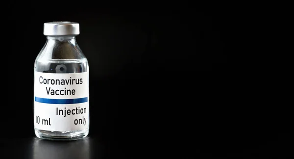 Coronavirus Covid 19 vaccine concept (own design, not real product) - small glass bottle with silver cap, closeup detail on black background