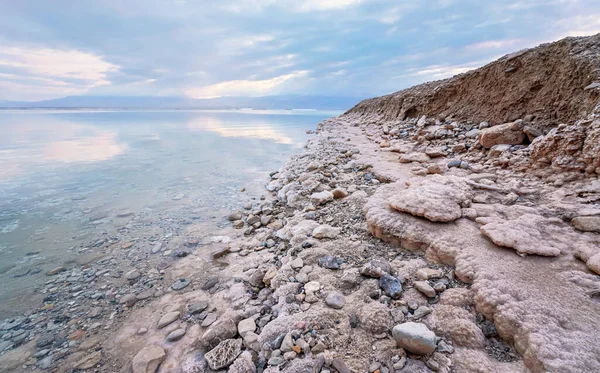 Sabbia e pietre ricoperte di sale cristallino sulla riva del Mar Morto, acqua limpida vicino - scenario tipico della spiaggia di Ein Bokek, Israele — Foto Stock