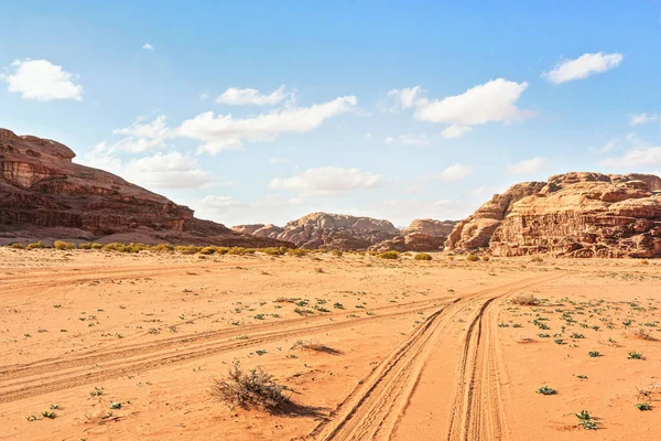 Macizos rocosos en el desierto de arena roja, pistas de vehículos tierra, cielo nublado brillante en el fondo, paisajes típicos en Wadi Rum, Jordania —  Fotos de Stock