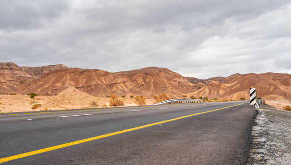 Modern asphalt highway leading through desert landscape in Southern region of Israel, cloudy sky above