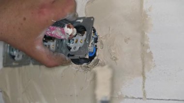 Erkek inşaat işçisi, çıplak duvara havan topu macunuyla elektrik prizleri yerleştiriyor. Delikleri sadece küçük kepçelerle dolduruyor.