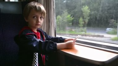 Cute boy traveling by train looking through window and holding the tickets