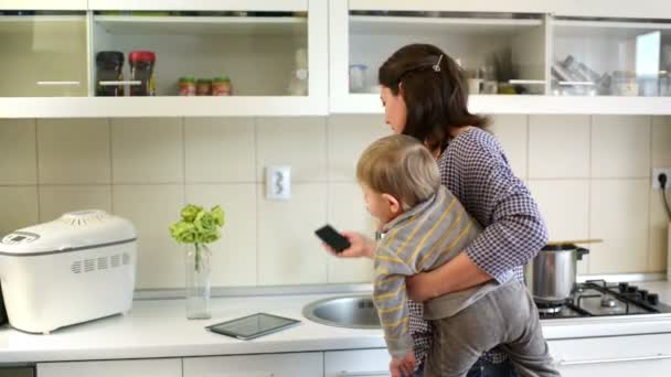 美しい若い母親の料理 デジタル タブレットを使用して 電話の会話を持って台所仕事をして赤ちゃんの世話をします 幸せな主婦 — ストック動画