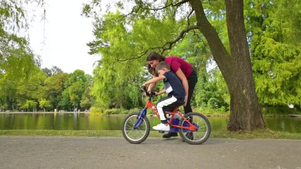 公園で自転車に乗るように彼の小さな息子を教える若い美しい母親 — ストック動画