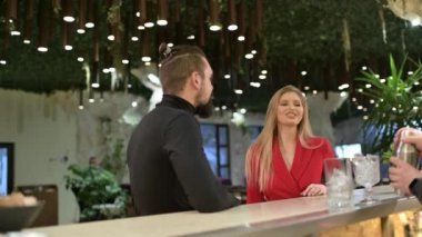 Genç çift, bistro barda güzel bir kadınla buluşmaktan zevk alıyor. Barmen ön planda kokteyl hazırlıyor.