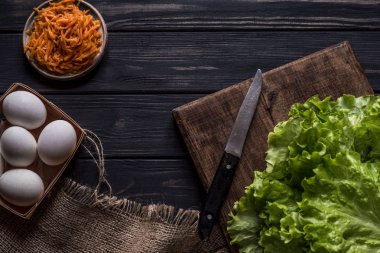 marul yaprakları ve bir bıçak üzerinde kahverengi ahşap masa, yumurta, havuç, siyah ahşap zemin masa örtüsü