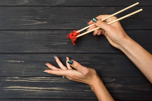 Yemek çubukları ve Turşu Zencefil bir siyah ahşap arka plan üzerinde tutan eller