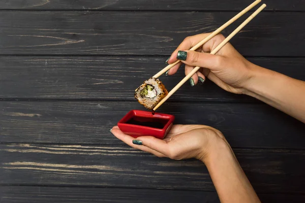 siyah bir ahşap zemin üzerine kırmızı bir kasede suşi ve soya sosu çubuklarla holding eller