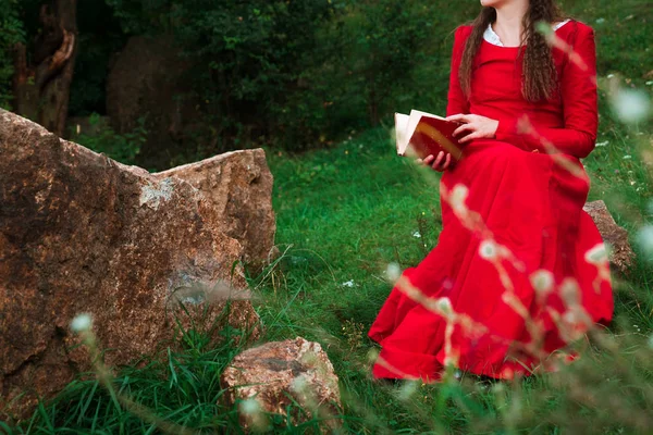girl in red historical dress reading a book in the park