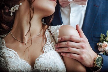 Mavi takım elbiseli damat geline ve kristal küpeli geline sarılıyor.