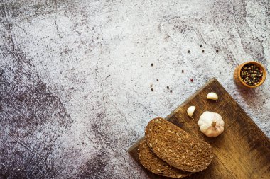 Çavdar ekmeği, sarımsaklı ve baharatlı kahverengi ahşap bir tahta üzerinde gri arka planda.