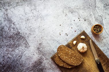 Çavdar ekmeği sarımsaklı, otlu ve baharatlı kahverengi ahşap bir tahtada gri bir zemin üzerinde