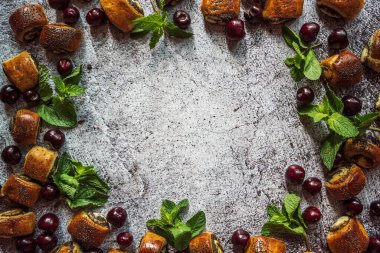 Gri arkaplan, çörekler, haşhaş tohumları, kirazlar ve nane 1 ile çerçevelenmiş.