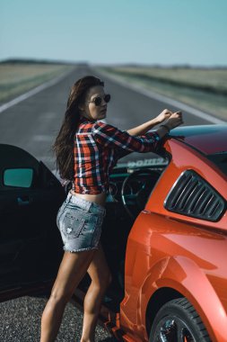 kısa şort giymiş güzel esmer kız ve kırmızı spor araba yakın güneş gözlüğü ile bir gömlek