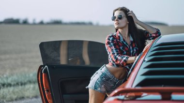 kısa şort giymiş güzel esmer kız ve kırmızı spor araba yakın güneş gözlüğü ile bir gömlek