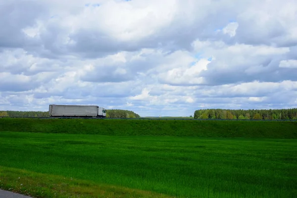 Semi truck drives through a picturesque place on the highway, big beautiful clouds and green fields