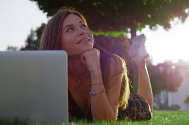 Parkta yeşil çimlerin üzerinde dizüstü bilgisayar kullanan genç bir kadın. Boş zaman aktivite kavramı. 
